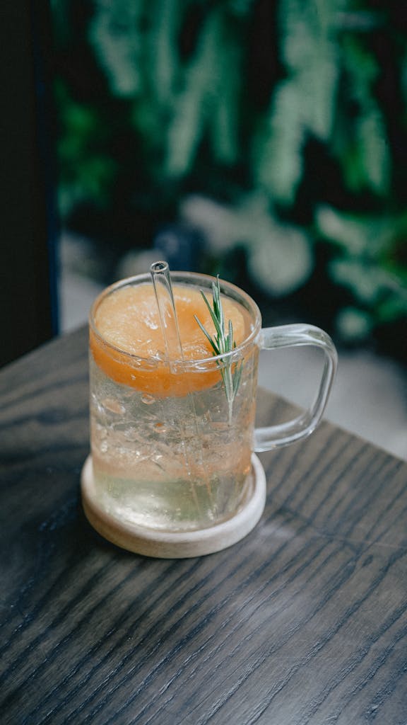 Chilled soda with citrus slice and rosemary in a glass on wooden table.